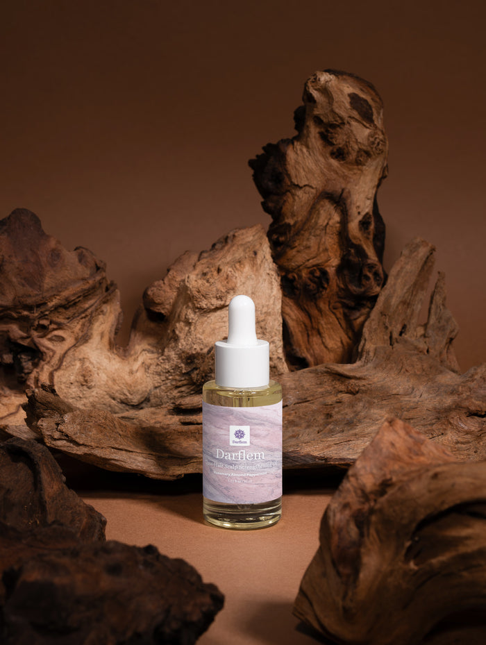 Darflem Rosemary Root Renewal Oil bottle among driftwood on a warm brown backdrop